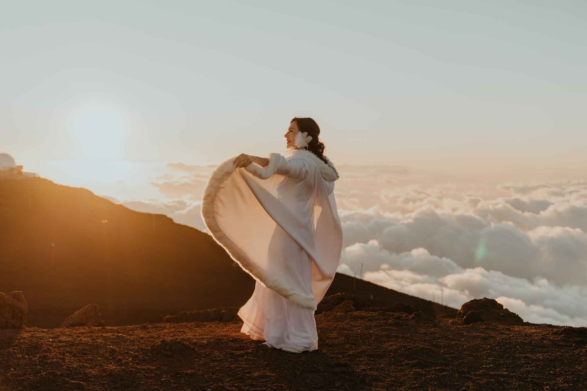 Bride in a white cape twirling above the clouds at Haleakalā summit at sunrise, Maui