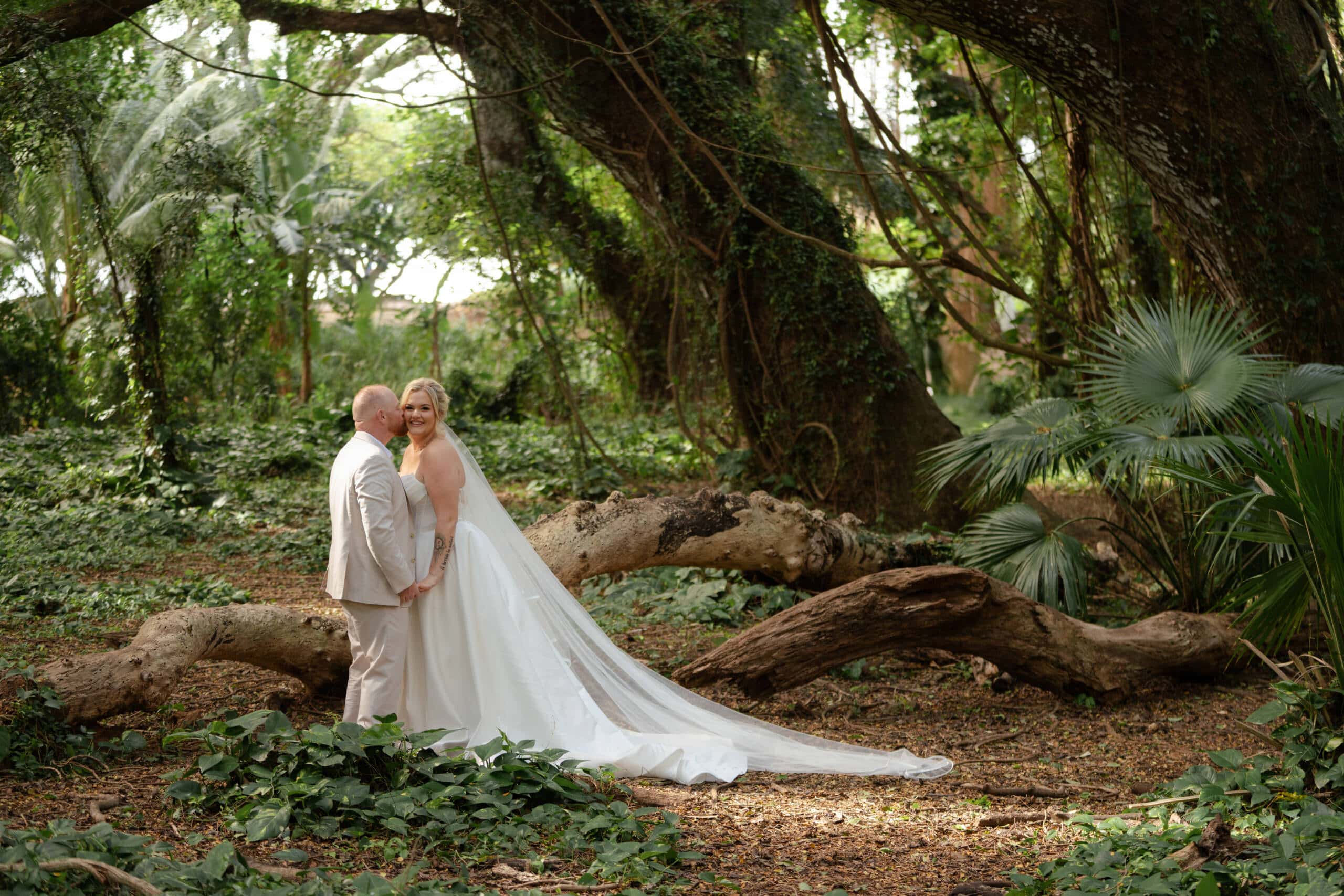 Bride and groom sharing a tender moment surrounded by lush tropical forest with dramatic banyan tree roots