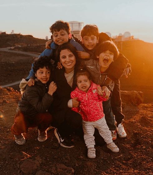 Family portrait at sunset on a Hawaii volcanic ridge — mother crouching with five joyful children, observatory domes in the background, golden hour light.